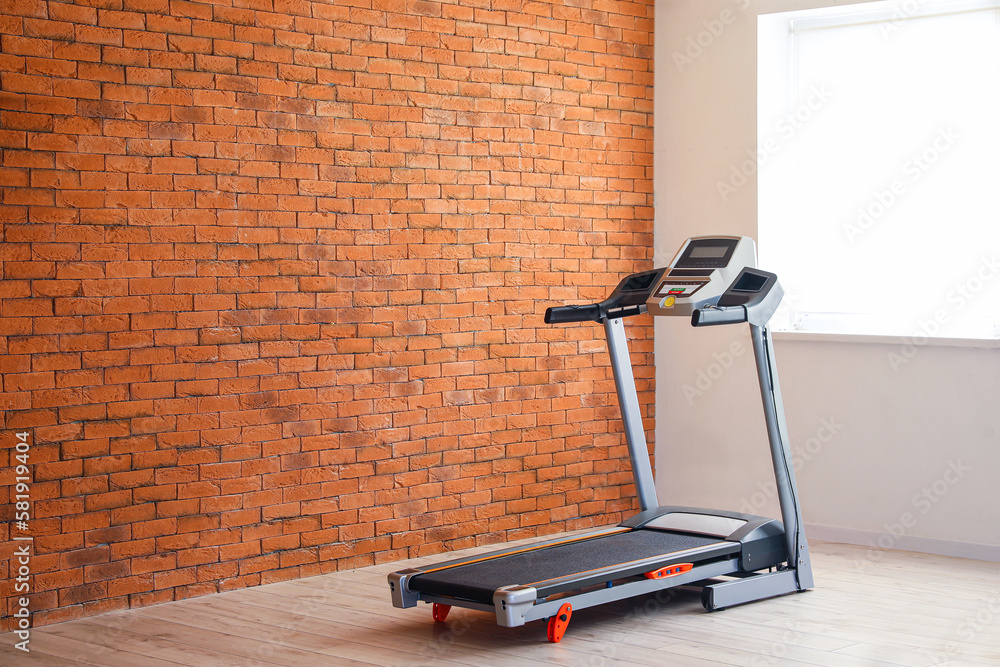 Interior of room with modern treadmill near brick wall