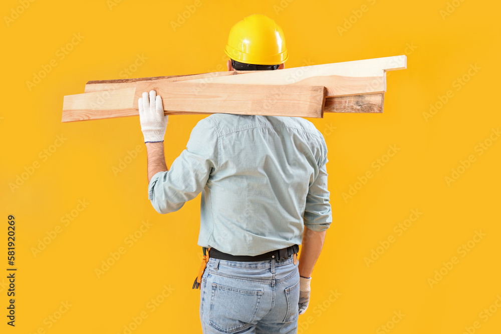 Male carpenter with wooden planks on yellow background, back view