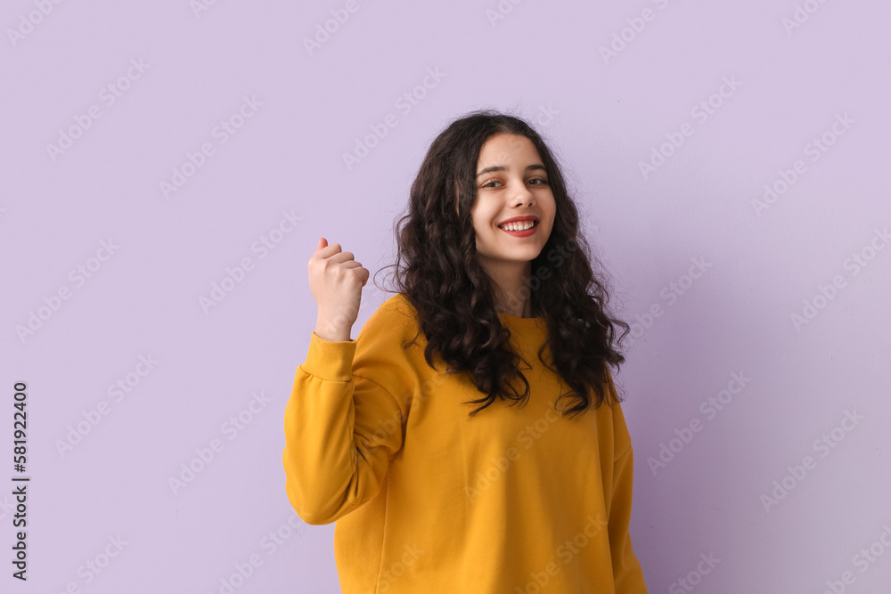 Teenage girl in yellow sweatshirt showing fist on lilac background