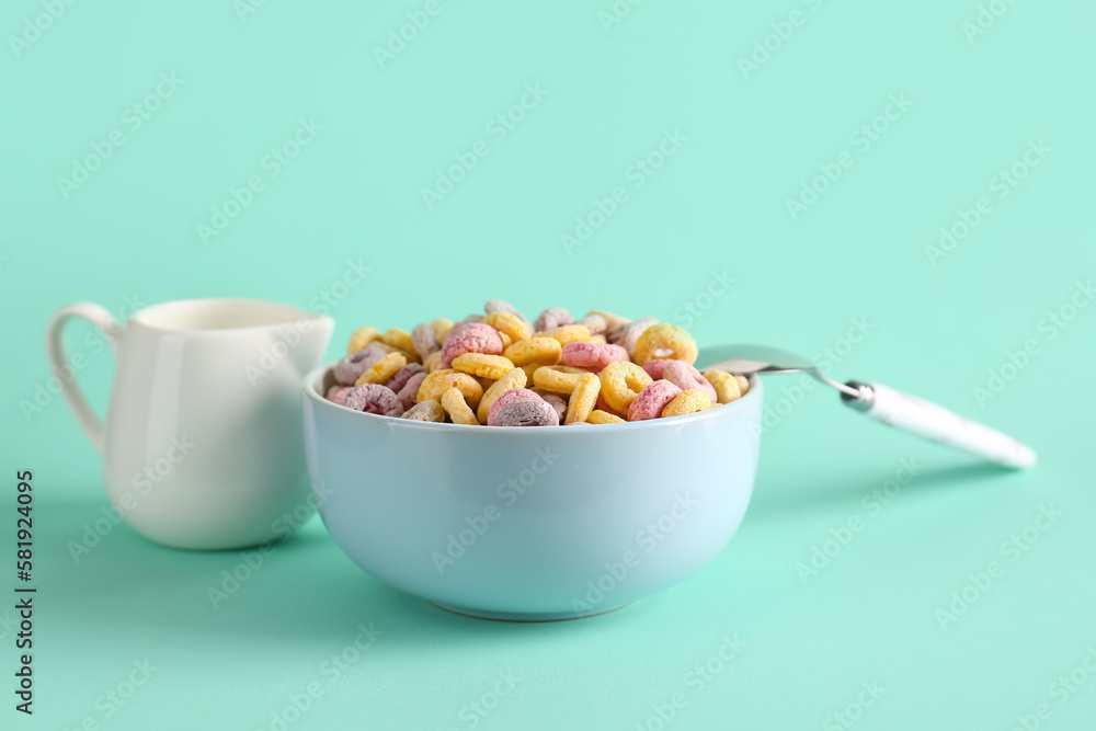 Bowl of colorful cereal rings and pitcher with milk on turquoise background