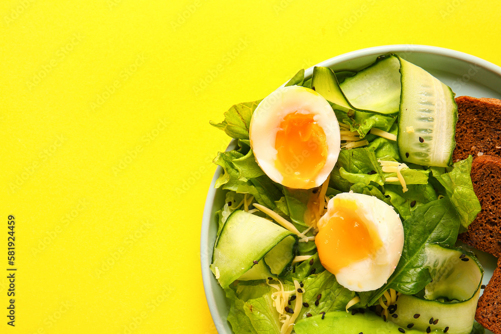 Plate of delicious salad with boiled eggs and avocado on yellow background