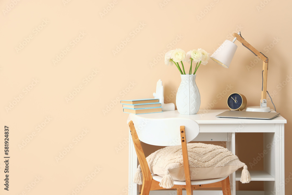 Workplace with ranunculus flowers in vase and lamp near beige wall