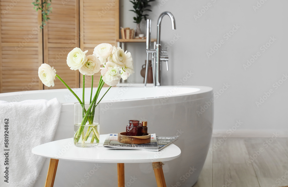 Vase with ranunculus flowers and magazines on table in bathroom