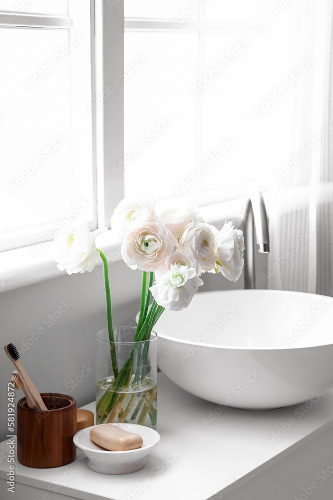 Vase with ranunculus flowers and sink on table in bathroom