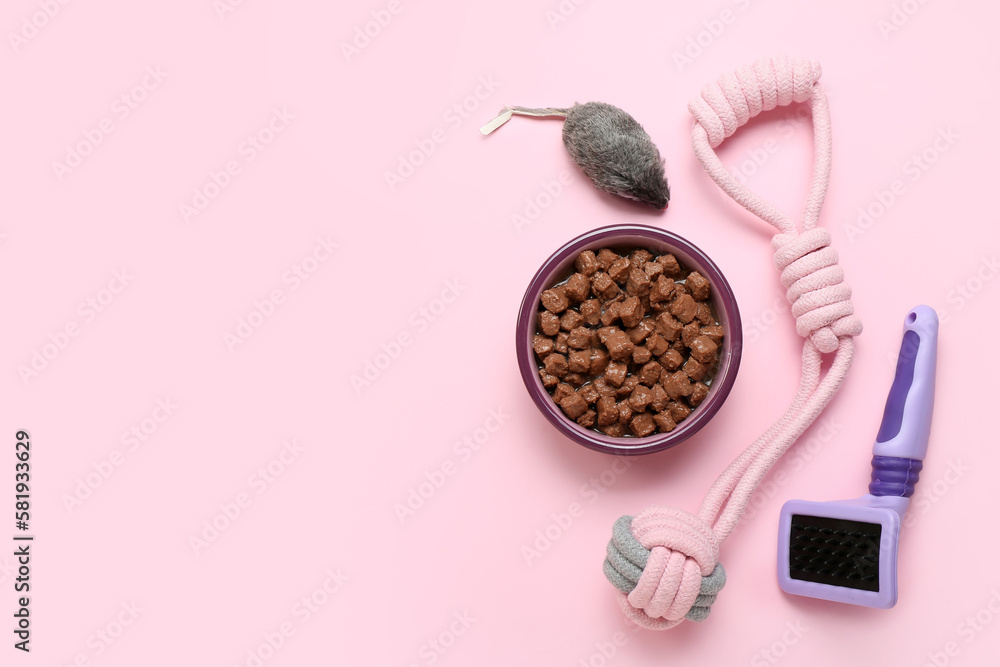 Bowl of wet pet food, grooming brush and toys on pink background