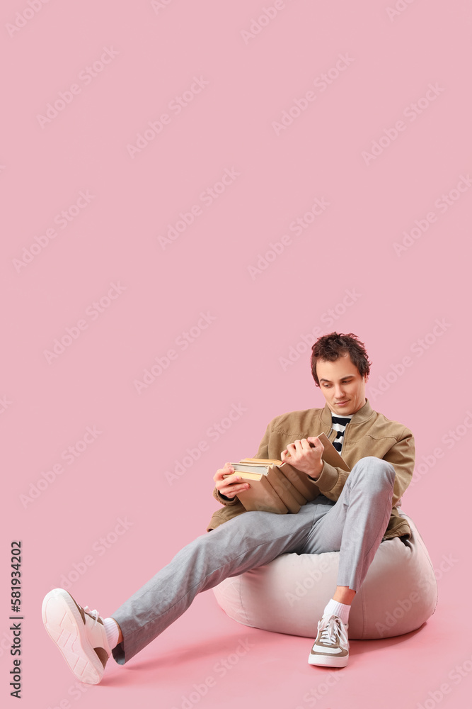 Young man reading book on pink background