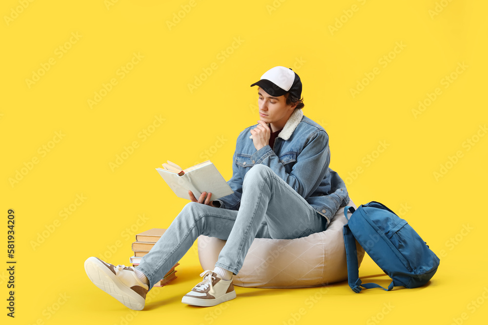 Male student reading book on yellow background