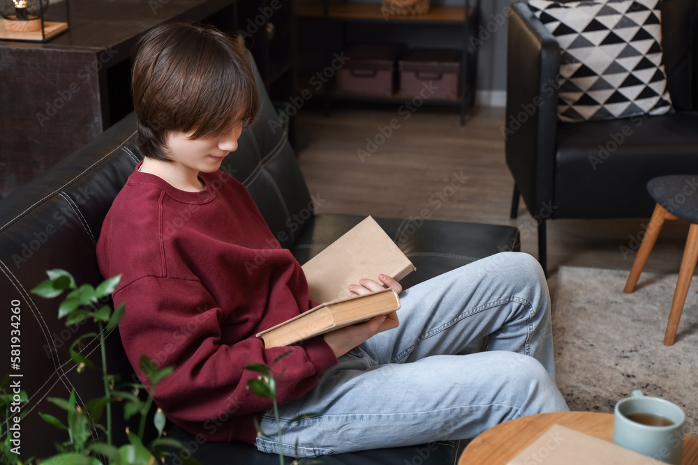 Teenage boy with books sitting on sofa at home late in evening