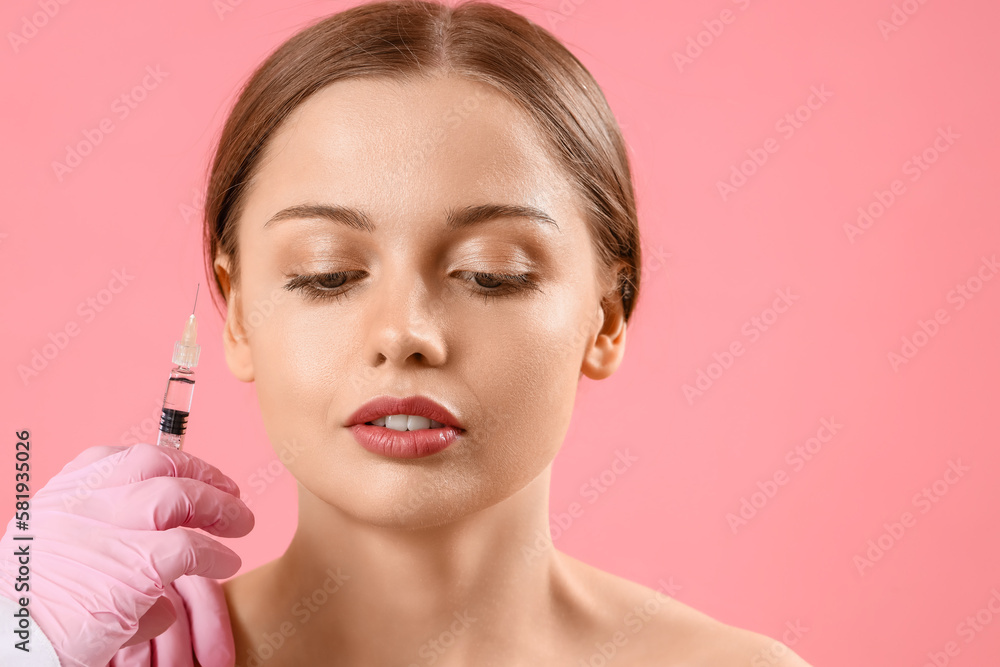 Young woman receiving filler injection in face against pink background