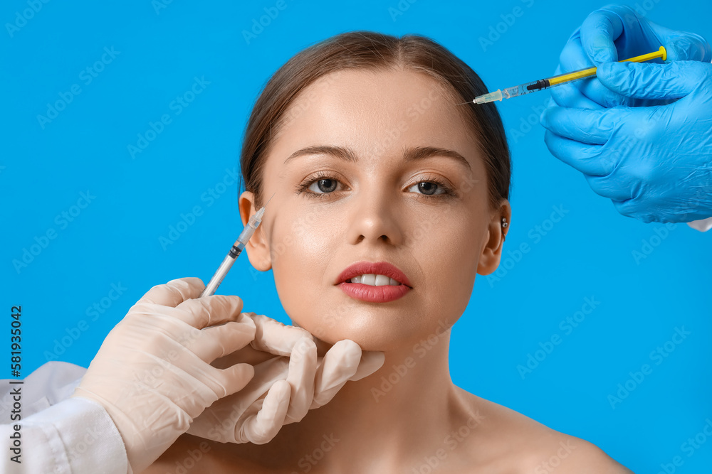 Young woman receiving filler injections in face against blue background