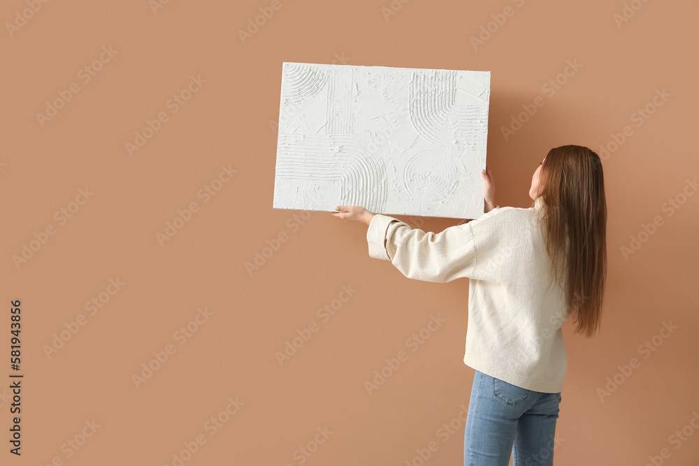 Young woman hanging painting on beige wall