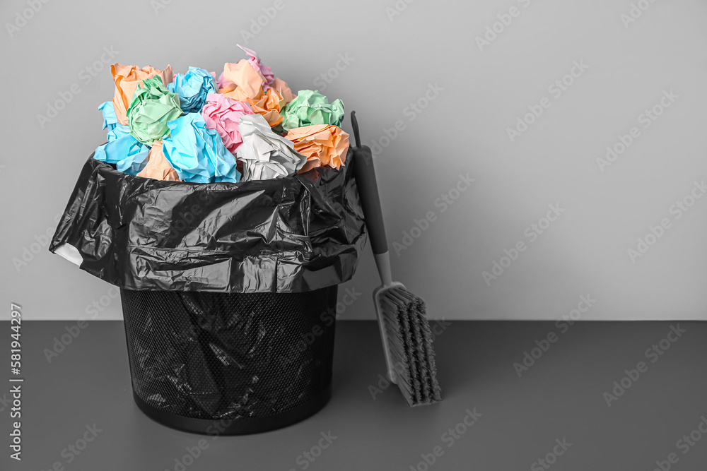 Rubbish bin with crumpled paper and brush near grey wall