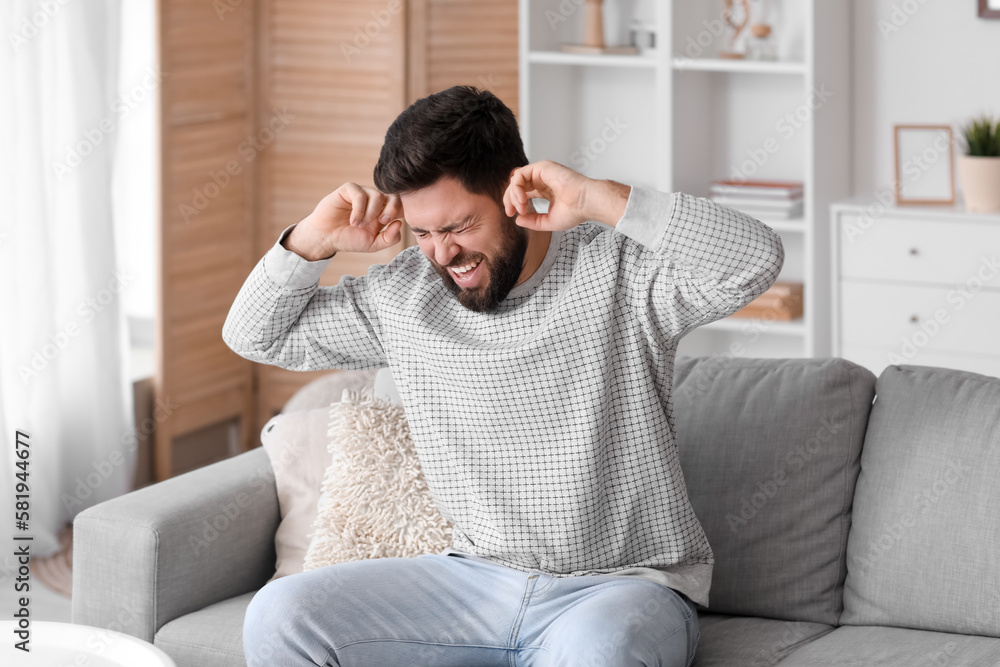 Angry young man suffering from loud noise at home