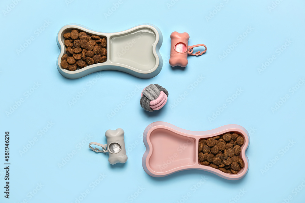 Bowls of dry pet food, ball and waste bags on color background