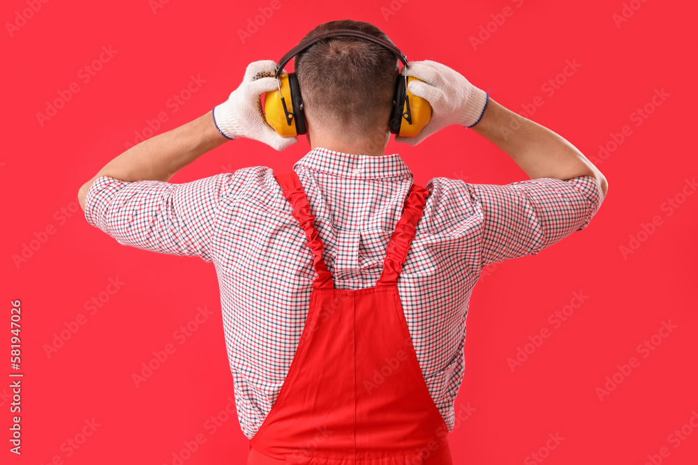 Mature carpenter in hearing protectors on red background, back view