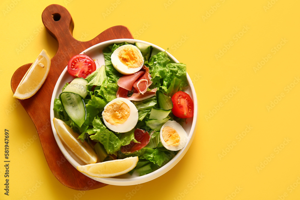 Board with plate of delicious salad on yellow background