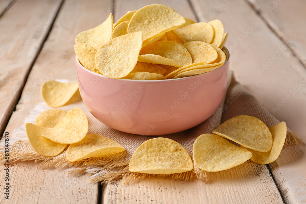 Bowl with delicious potato chips on white wooden background