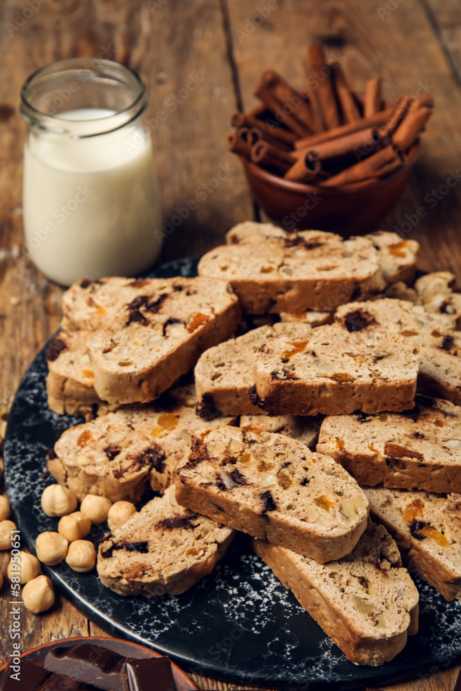 Board with delicious biscotti cookies, hazelnuts and glass of milk on wooden background