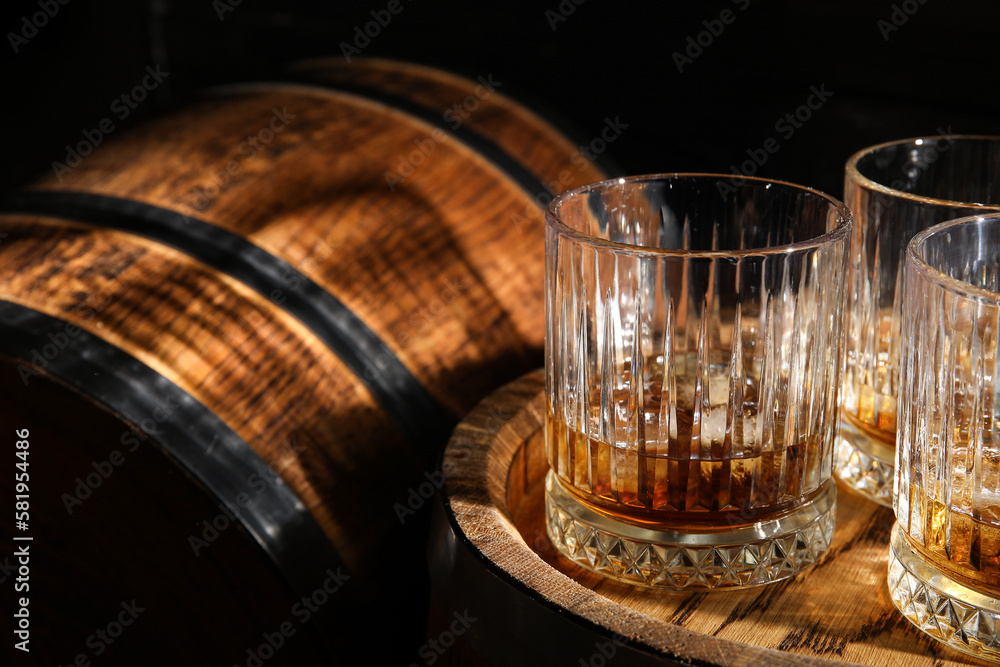 Oak barrels with glasses of cold whiskey on dark wooden background