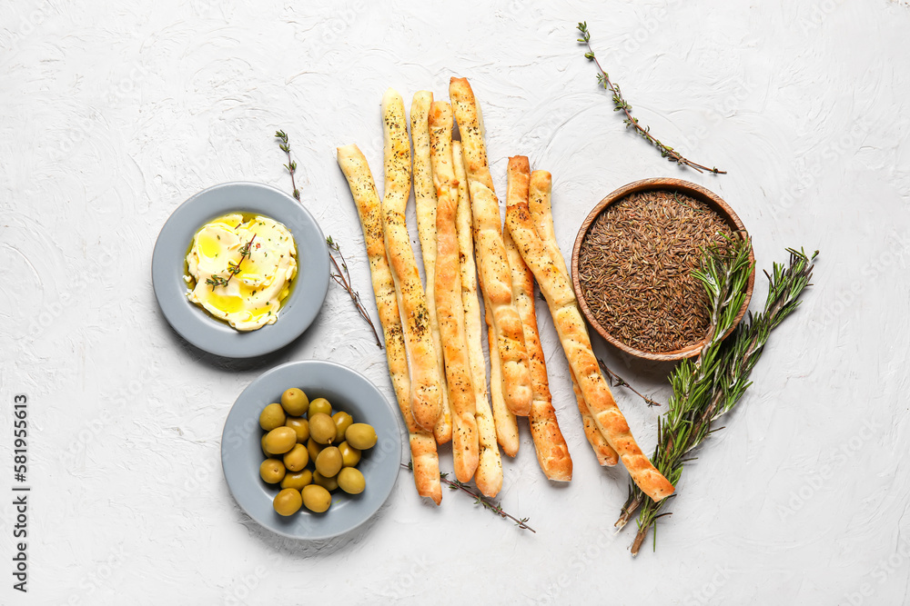 Composition with tasty Italian Grissini, thyme, butter and green olives on light background