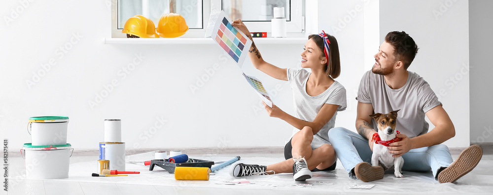 Happy young couple with cute dog choosing color of paint for repair in their new house