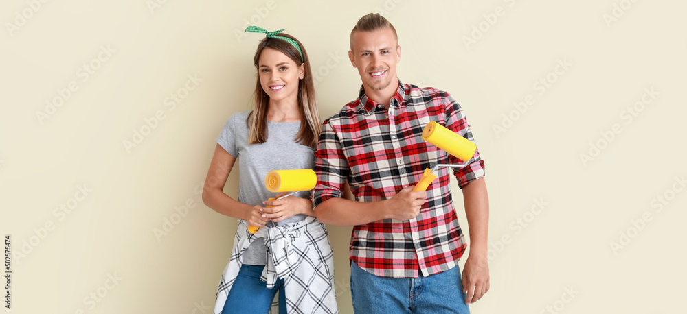 Happy young couple with paint rollers near beige wall