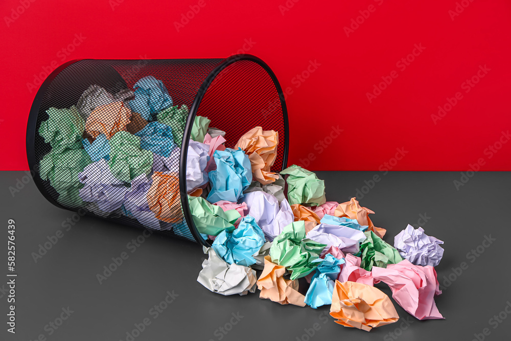 Rubbish bin with crumpled paper near red wall