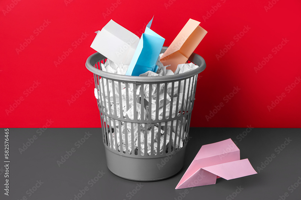 Rubbish bin with paper garbage near red wall