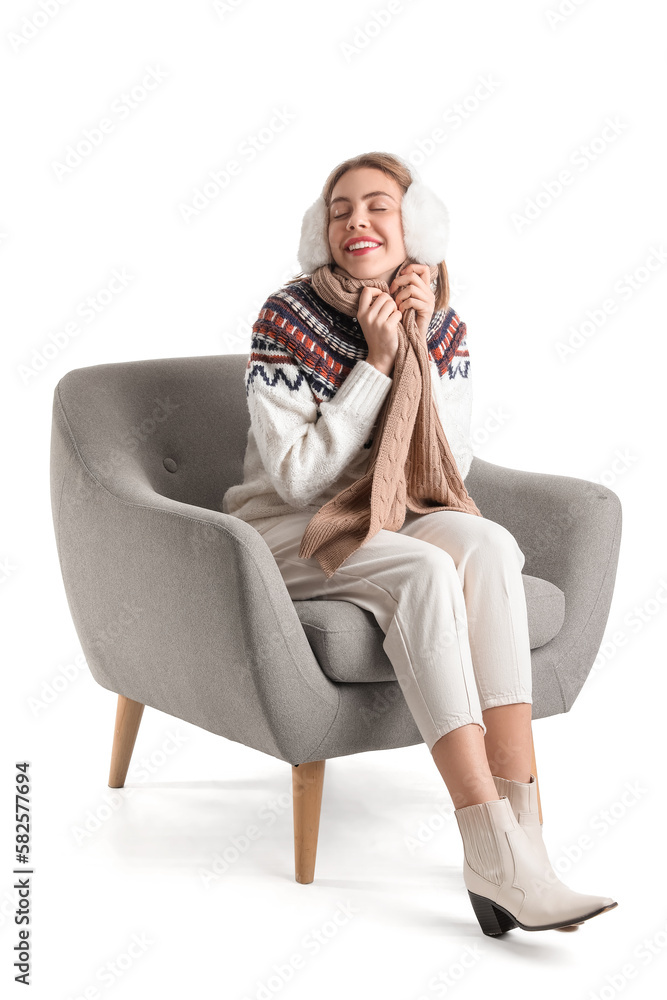 Young woman with earmuffs sitting in grey armchair on white background