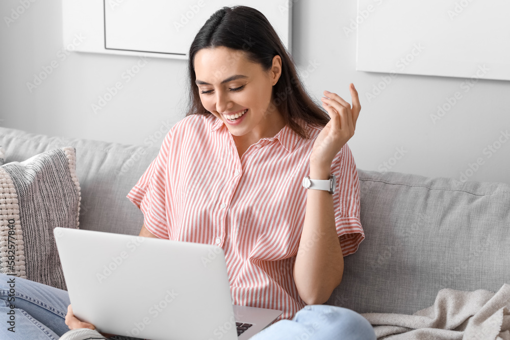 Young woman with wristwatch using laptop on sofa at home