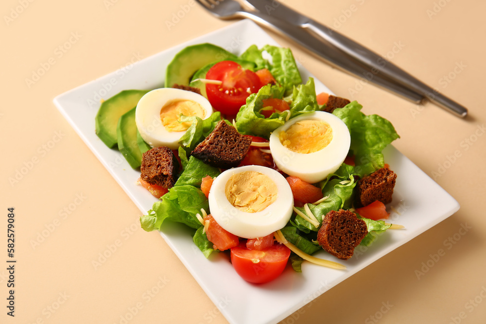 Plate of delicious salad with boiled eggs and salmon on beige background