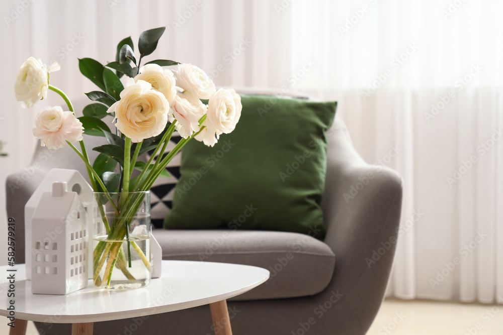 Vase with ranunculus flowers and house candle holders on table in living room