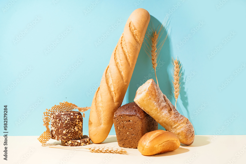 Loaves of different bread and wheat ears on beige table near blue wall