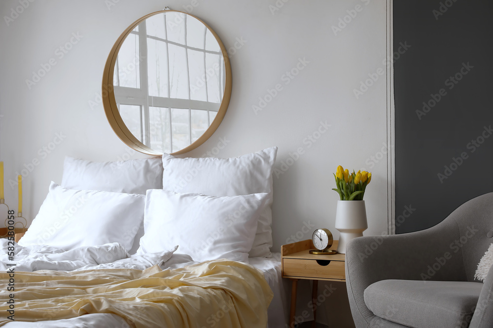 Interior of light bedroom with mirror and tulips in vase