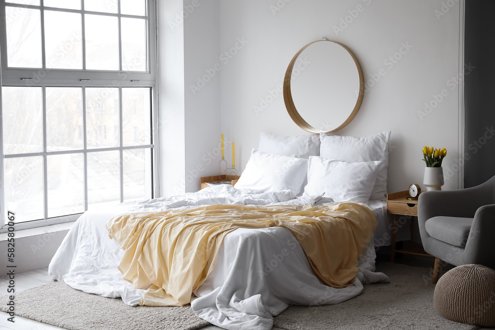 Interior of light bedroom with mirror and tulips in vase