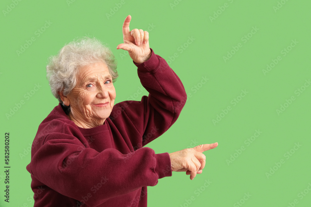 Senior woman showing loser gesture on green background