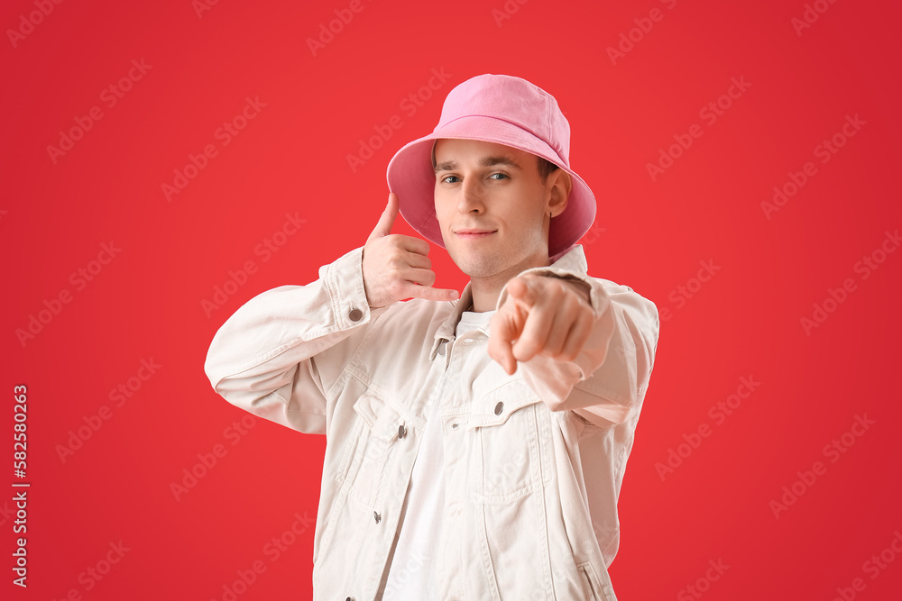 Cool young man showing  call me  gesture on red background