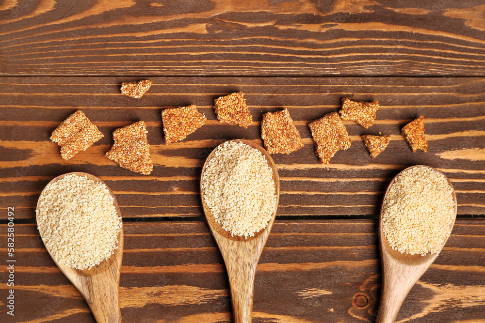 Spoons with sesame seeds and tasty kozinaki on wooden background, closeup