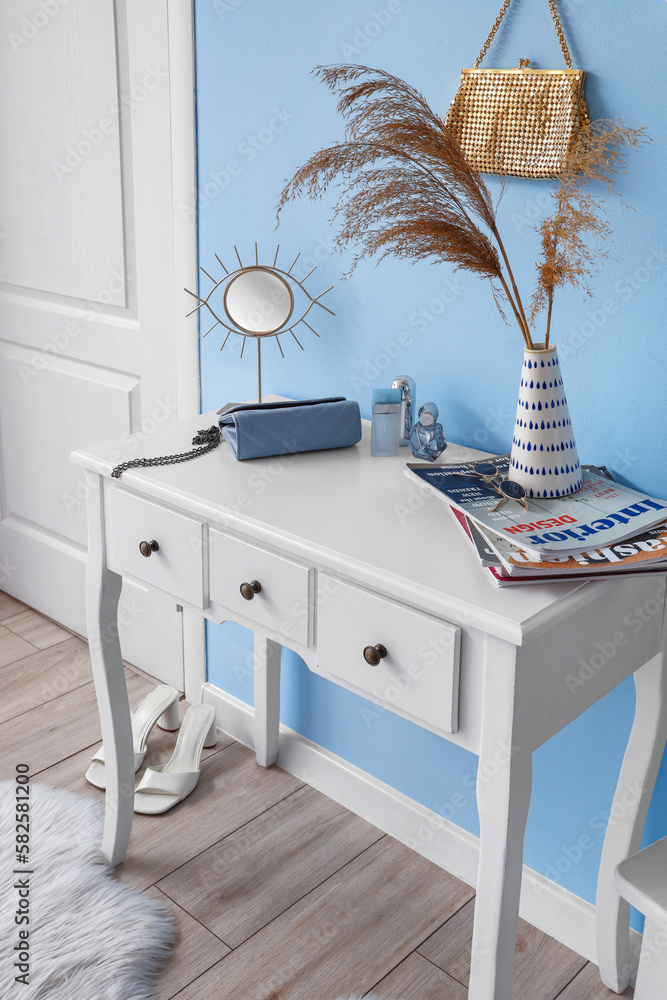 Vase with pampas grass, magazines, accessories and mirror on table in hall