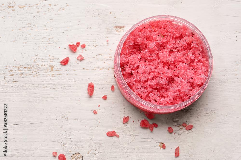 Jar of body scrub and sea salt on light wooden background