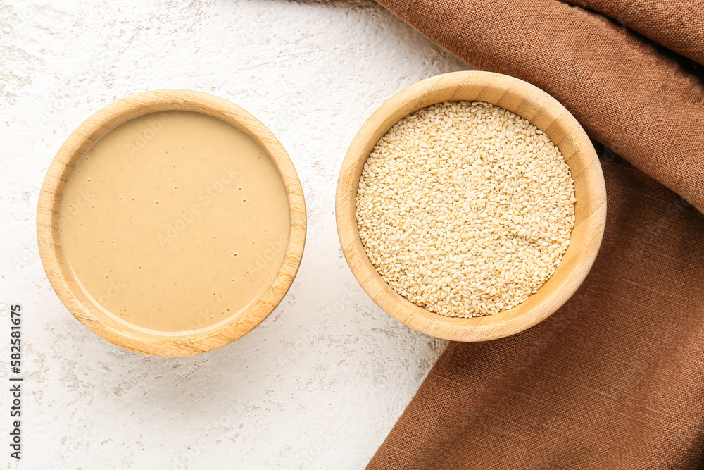 Wooden bowls with tasty tahini and sesame seeds on light background