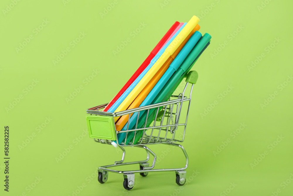 Shopping cart with pencils on green background