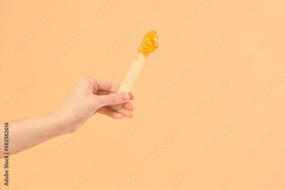 Female hand holding spatula with sugaring paste on beige background