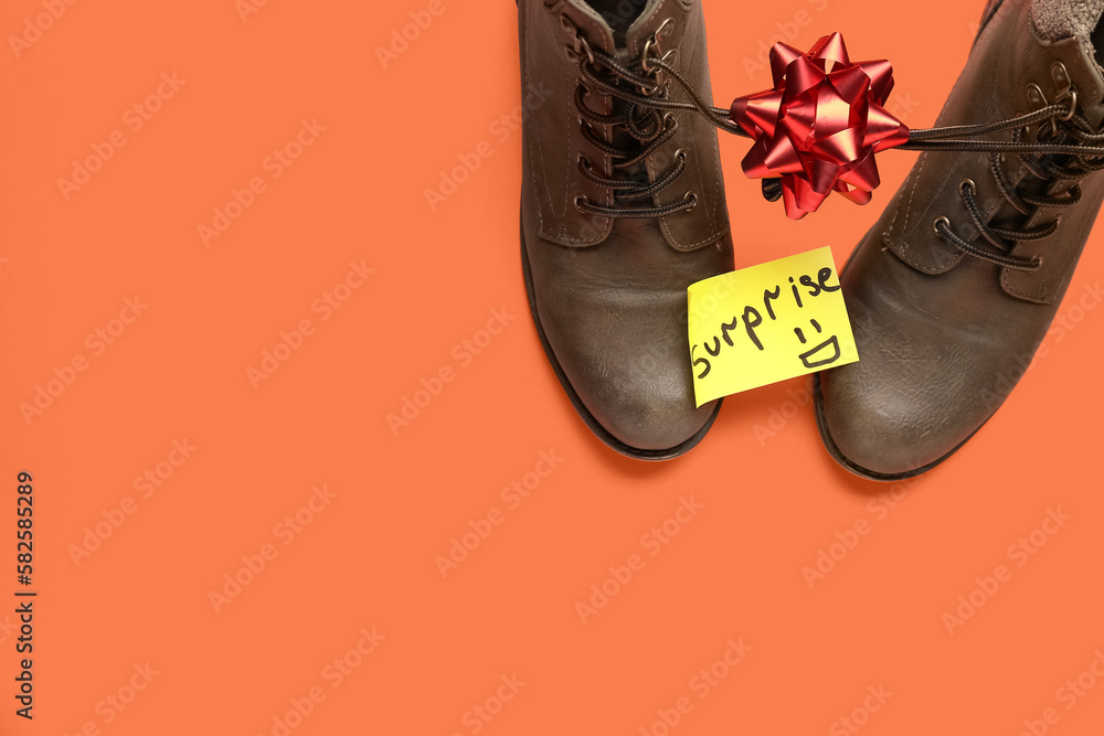 Paper with word SURPRISE, boots and bow on red background. April Fools Day celebration