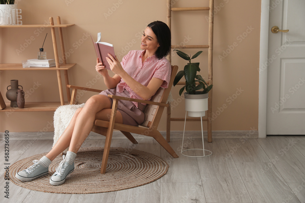 Beautiful woman reading book in wooden armchair at home