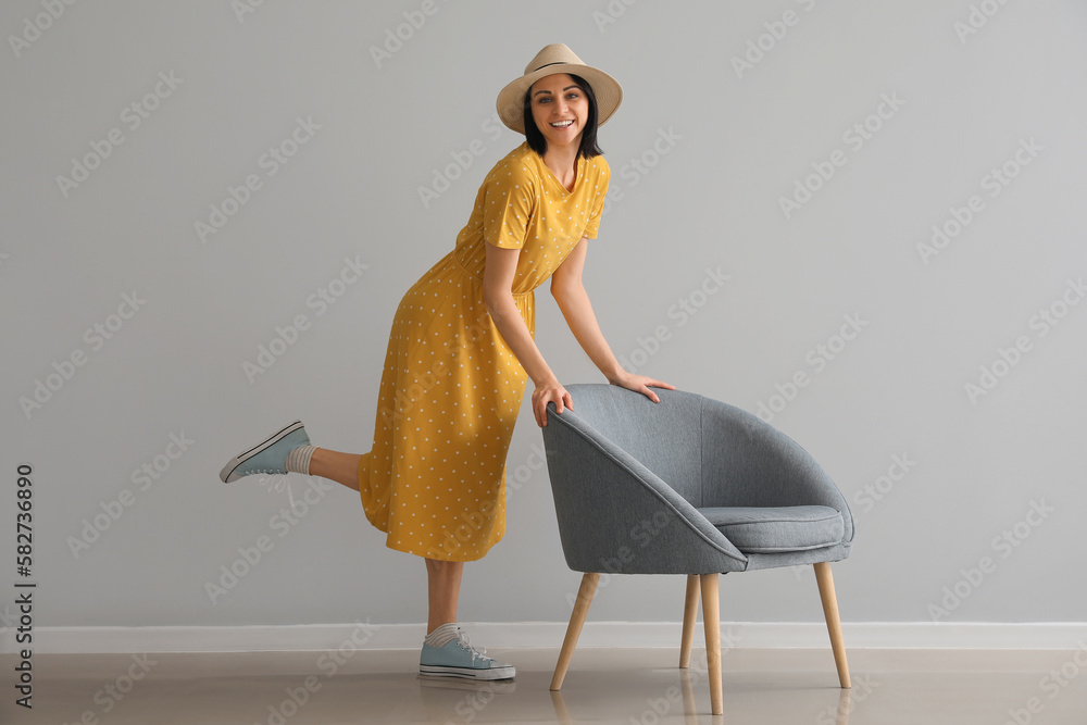 Beautiful woman beside soft armchair near grey wall