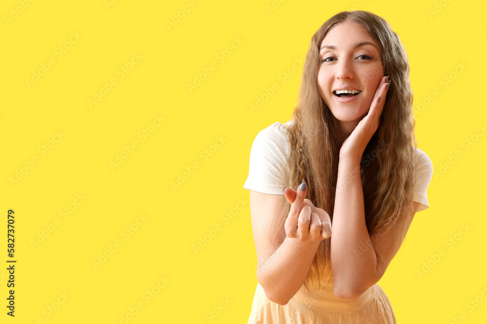 Beautiful young woman making heart shape with her fingers on yellow background