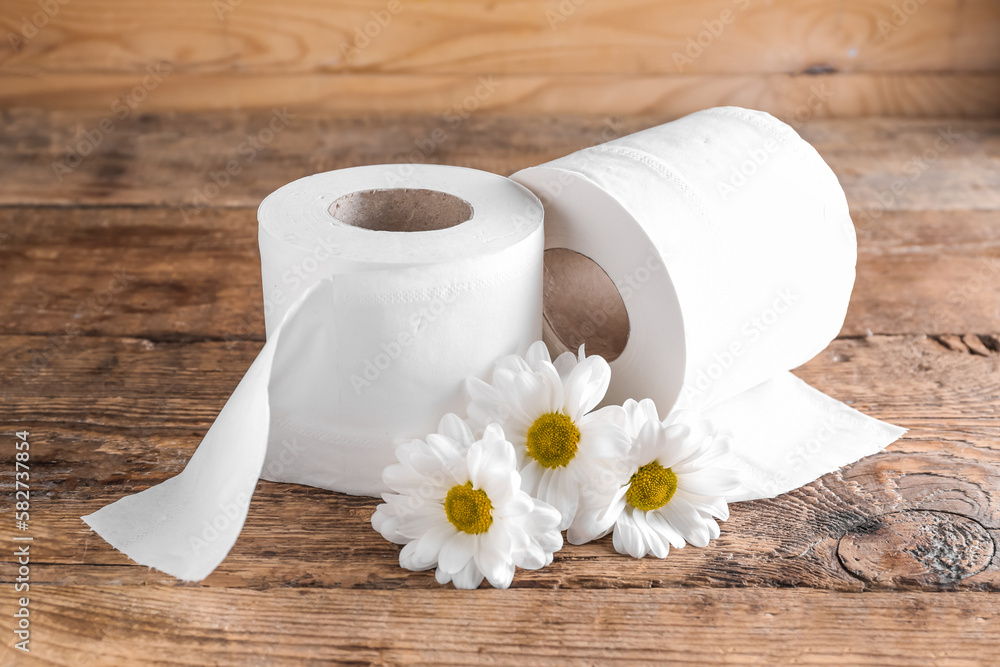 Rolls of toilet paper and chamomile flowers on wooden background