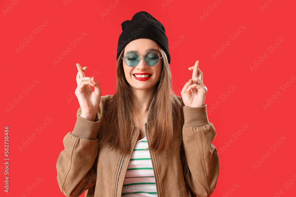 Stylish young woman crossing fingers on red background