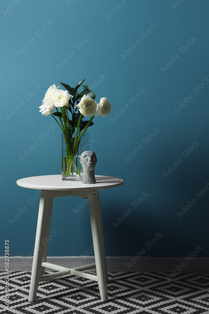 Vase with ranunculus flowers and decor on table near blue wall